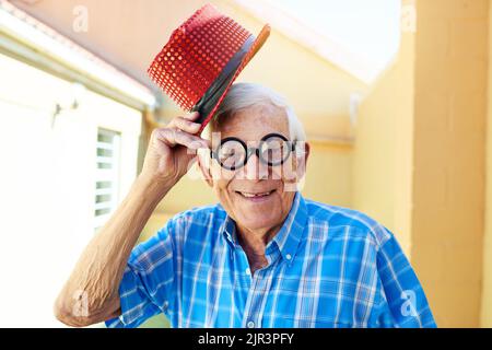 Ich ziehe meinen Hut ab vor dir, mein Herr. Ein unbeschwerter älterer Mann, der eine funky Brille und einen Hut trägt, während er für die Kamera in einem Gebäude posiert. Stockfoto