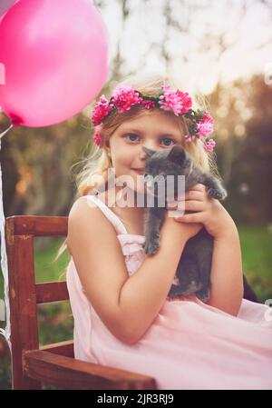 Bester Geburtstag aller Zeiten. Ein glückliches kleines Mädchen, das ein Kätzchen in der Hand hält und draußen in der Natur auf die Kamera schaut. Stockfoto