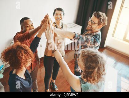 Wir feiern unsere Leistungen gemeinsam. Kreative Mitarbeiter geben sich gegenseitig im Büro einen High-Five. Stockfoto