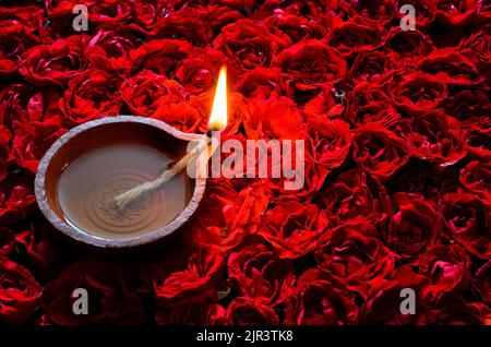 Dekorative rote Rose Blume Rangoli für Diwali Festival mit Ton Diya Lampe mit Flamme beleuchtet. Stockfoto