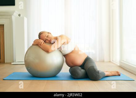 Eine Schwangere, die zu Hause mit einem Gymnastikball trainiert, macht ihre Schwangerschaft fit und stressfrei. Stockfoto