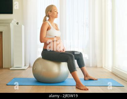 Gesund bleiben für eine stressfreie Schwangerschaft. Eine Schwangerin trainiert zu Hause mit einem Gymnastikball. Stockfoto