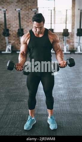 Ein junger Mann, der mit Hanteln im Fitnessstudio arbeitet. Stockfoto