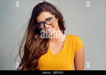 Sie hat ein Lächeln, das den Raum erhellt. Studioportrait einer attraktiven jungen Frau, die vor grauem Hintergrund posiert. Stockfoto