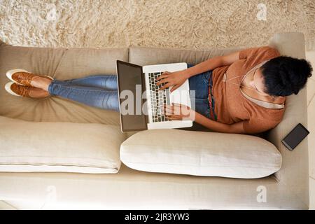Bloggen zu Hause auf die komfortablste Art und Weise. Eine unkenntliche Frau, die zu Hause einen Laptop benutzt. Stockfoto