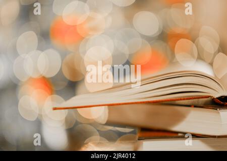 Weihnachtsbücher.Stapel von Büchern auf dem Tisch auf glänzenden funkelnden Girlanden Hintergrund.gemütliche Lesung in der Wintersaison.Weihnachtsgeschichten, Geschichten und Stockfoto