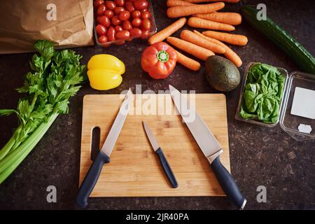 Überspringen Sie Ihre Ernährung, nur gesund essen. Eine Aufnahme aus einer Auswahl frischer Zutaten, die auf einem Schneidebrett auf einer Küchentheke angeordnet sind. Stockfoto