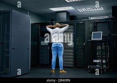 Hinter den Kulissen einer Fehlermeldung. Rückansicht eines IT-Technikers, der Schwierigkeiten hat, einen Computer in einem Rechenzentrum zu reparieren. Stockfoto
