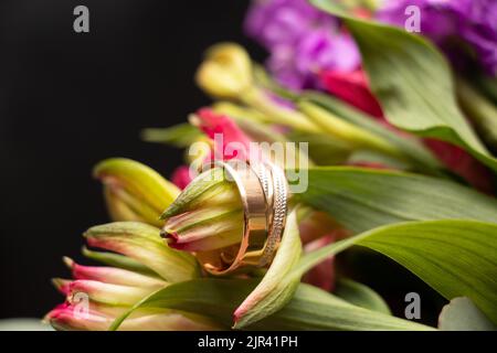 Hochzeit Goldringe der Braut und des Bräutigams liegen auf dem Hintergrund eines Blumenstraußes der Braut, Goldringe bei der Hochzeit Stockfoto