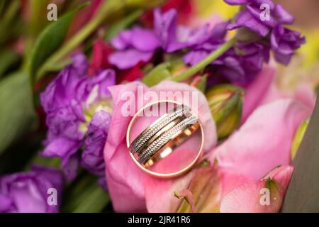 Hochzeit Goldringe der Braut und des Bräutigams liegen auf dem Hintergrund eines Blumenstraußes der Braut, Goldringe bei der Hochzeit Stockfoto