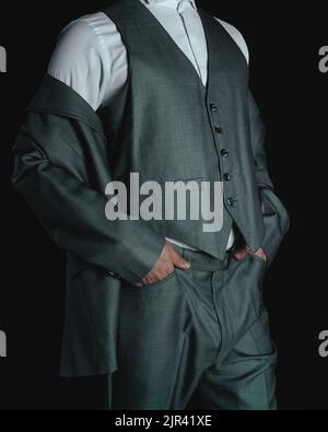 Körper eines Mannes in einem grauen Anzug. Eleganter grauer Anzug. Geschäftsmann posiert auf einem dunklen Hintergrund. Mann, der in Anzug gekleidet ist und seinen Anzug modelliert. Hochwertige Fotos Stockfoto