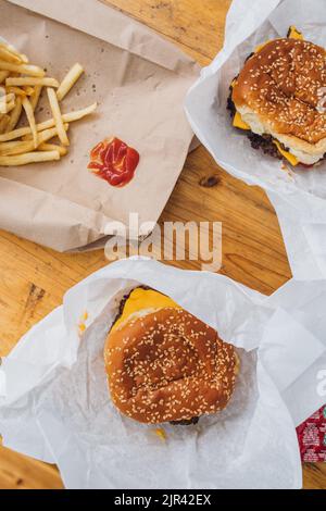 Blick auf den Tisch im Freien mit Pommes frites zum Teilen und zwei Cheeseburgern auf weißem Papier Stockfoto