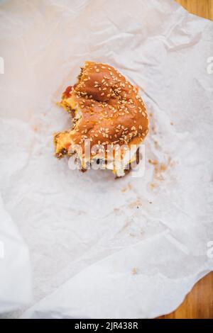 Halbgessene Cheeseburger mit Sesambrötchen auf weißem Papier Stockfoto