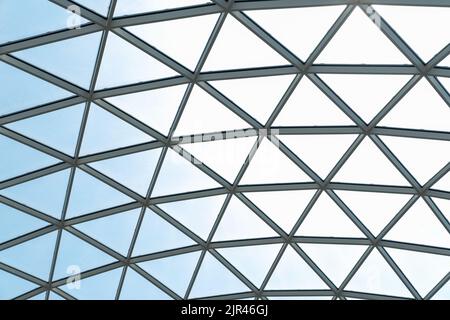 Architektonische Glasstruktur mit geometrischem Dreiecksmuster auf blauem Himmel. Stahlglas Dachwandkonstruktion transparentes Fenster mit Stockfoto