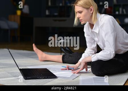 Frau sitzt mit ihrem Laptop auf dem Boden und arbeitet. Stockfoto