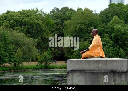 Boston, MA, USA - 16. Juli 2022: Ein Mann in orangefarbener Mönchskleidung meditiert in einem Park neben dem Charles River in Boston, MA, USA Stockfoto
