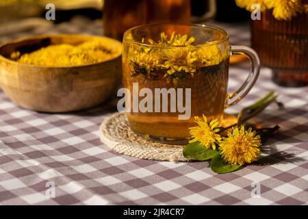 Der gesunde Tee aus der Nelken-Blume in einer Glastasse auf dem Tisch. Kräutermedizin köstlicher Tee aus Tisane mit frischen gelben Blüten in der Teetasse. Grüne Clearing Infusion Wildflowers umweltfreundliches Bio-Markenkonzept. Schöne Grußkarte für den internationalen Tee Tag Kräutergetränk Stockfoto