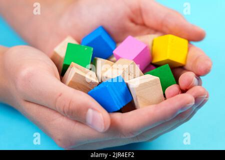 Pädagogische bunte Spielzeugblöcke aus Holz Nahaufnahme auf blauem Hintergrund in den Händen. Spielwürfel Stockfoto