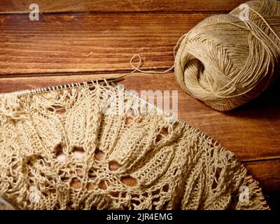 Prozess des Strickens. Stricknadeln, Schlaufen auf Stricknadeln, Strickstoff, Fadenknäuel, grobes Baumwoll- und Leinengarn, Holzhintergrund Stockfoto