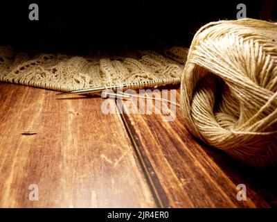 Durchbrochene Tischdecke beim Stricken. Stricknadeln, Schlaufen auf Stricknadeln, Strickstoff, Fadenknäuel, grobe Baumwolle und Leinen Stockfoto