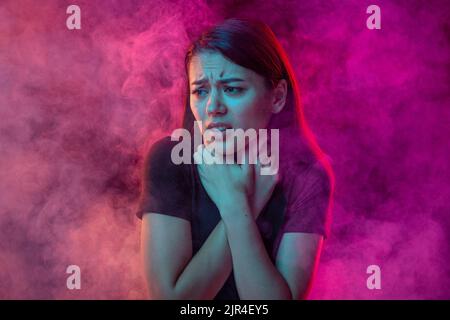 Ersticken Sie im Rauch. Ängstlicher junger Mann mit gestressten Emotionen isoliert über rosa Hintergrund mit Wolken aus Rauch. Konzept des Gesichtsausdrucks Stockfoto