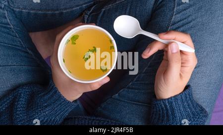 Hände mit einer Tasse zum Mitnehmen und Hühnerbrühe Stockfoto