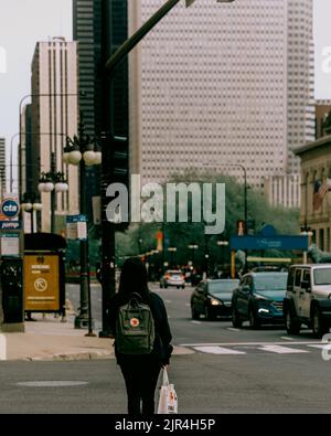 Eine vertikale Aufnahme eines asiatischen Mädchens, das von hinten mit einem Rucksack auf den Straßen Chicagos unterwegs ist Stockfoto