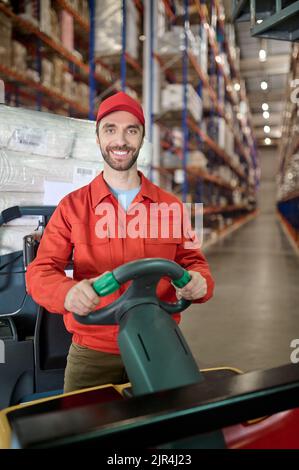 Fröhlicher Arbeiter, der Waren im Lager umherbewegt Stockfoto