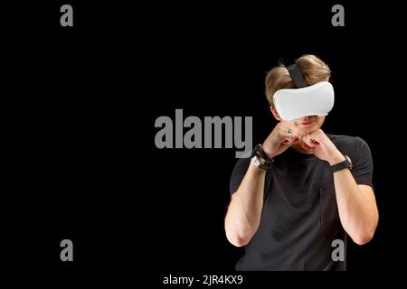 Junger Mann trägt Virtual Reality VR-Brille, Brille isoliert auf schwarzem Hintergrund. In Einer Metaverse Stockfoto