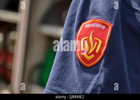 Niederländisches Feuerwehrabzeichen auf dem Hemd eines Feuerwehrmann. Niederländisches Gold- und rot besticktes Feuerwehrlogo auf der Schulterpartie eines blauen Hemdes. Stockfoto