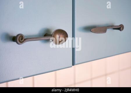 Küchengriffe in Form von Besteck wie Löffel, Messer und Gabeln auf grau-grün lackierten Schranktüren. Stockfoto