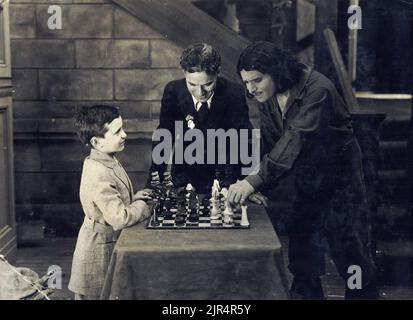 Douglas Fairbanks spielt Schach mit Samuel Reshevsky und Charlie Chaplin sieht sich das Spiel an, am Set des amerikanischen Stummfilms von Fairbanks die drei Musketiere. 1921. Stockfoto