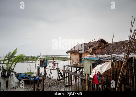 Kalabogi, Bangladesch. 18. August 2022. Ein Junge sah, wie er zur hängenden Toilette im Dorf Kalabogi in Khulna ging. Vor nicht allzu langer Zeit war Kalabogi, ein Küstendorf in Bangladesch, voller anbauflächiger Flächen, bis der steigende Meeresspiegel das Gebiet bis zur Bucht von Bengalen verschlang. Seit Ende 1990s ereignissen sich im Dorf häufige Wirbelstürme und Überschwemmungen. Im Jahr 2009 zerstörte ein großer Wirbelsturm namens Aila die 1.400 Kilometer Böschungen, 8.800 Kilometer Straßen und etwa 3 50.000 Hektar Ackerland des Landes. Mehrere hundert Menschen seien bei der Katastrophe getötet worden. Die Bauern von Kalabogi Stockfoto