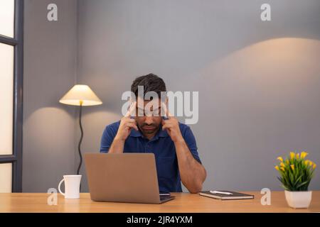 Gestresster freiberuflicher Mann, der im Home Office vor dem Laptop mit der Hand am Kopf sitzt Stockfoto