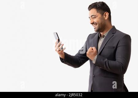 Aufgeregter junger Geschäftsmann, der das Handy anschaut Stockfoto