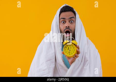 Porträt eines schockierten jungen Mannes mit Wecker auf gelbem Hintergrund Stockfoto