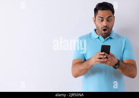 Porträt eines überraschten jungen Mannes, der mit Smartphone vor weißem Hintergrund steht Stockfoto
