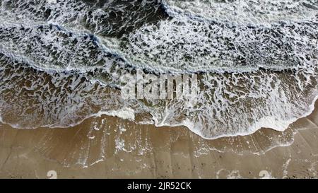Lufttrohnenblick Flug über wunderschöne Meereswellen und White Foam am Sand Beach. Top Blick auf fantastische erstaunliche natürliche Meer. Wasserstruktur. Landschaft tropischer Strand und Küste. Sommerlandschaft Stockfoto