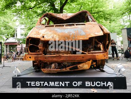 Berlin, Deutschland. 22. August 2022. „Testament of Bucha“ („Testament of Butscha“) steht unter dem zerstörten Auto, das auf dem George-Grosz-Platz in Charlottenburg steht. Es ist das Auto, in dem vier ukrainische Frauen auf der Flucht vom russischen Militär angeschossen wurden und starben. Die Ausstellung ist bis zum 15. September 2022 zu sehen. Quelle: Annette Riedl/dpa/Alamy Live News Stockfoto