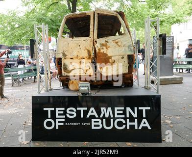 Berlin, Deutschland. 22. August 2022. „Testament of Bucha“ („Testament of Butscha“) steht unter dem zerstörten Auto, das auf dem George-Grosz-Platz in Charlottenburg steht. Es ist das Auto, in dem vier ukrainische Frauen auf der Flucht vom russischen Militär angeschossen wurden und starben. Die Ausstellung ist bis zum 15. September 2022 zu sehen. Quelle: Annette Riedl/dpa/Alamy Live News Stockfoto