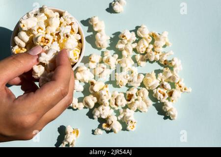 Hand nimmt Salz Popcorn aus Handwerk Papierbecher. Stockfoto