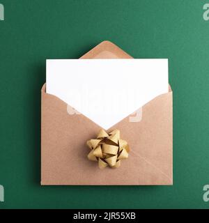 Öffnen Sie den festlichen Kraftpapier-Umschlag mit einer sauberen Karte, und legen Sie den Text auf grünen Hintergrund. Flach liegend. Stockfoto