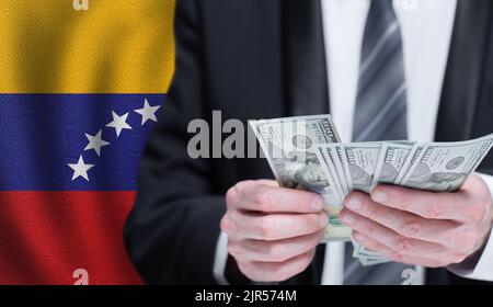 Hände, die Dollargeld auf der Flagge Venezuelas halten Stockfoto