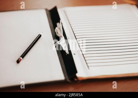 Auf dem Holztisch befindet sich ein sauberes Notizbuch für Notizen und ein Bleistift. Zeit für Kreativität und Inspiration. Ein sauberer Schiefer. Stockfoto