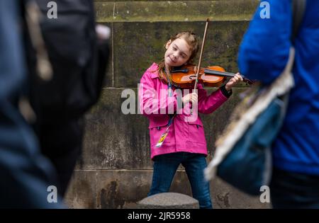 Royal Mile, Edinburgh, Schottland, Großbritannien, 22.. August 2022. Randdarsteller: Eine sehr junge Straßenmusikerin namens Emma Deimal spielt vor der St Giles Cathedral und spielt Geige. Kredit: Sally Anderson/Alamy Live Nachrichten Stockfoto