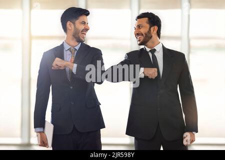 Firmenmitarbeiter im formellen Business-Anzug stehen mit ihren Ellbogen verbunden, lächelnd. Stockfoto
