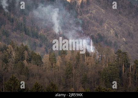 Örtlich begrenztes Wildfeuer, bei dem der Hubschrauber Wasser abtropft, indem er einen Wassereimer verwendet, der an einer langen Linie unter dem Hubschrauber befestigt ist Stockfoto