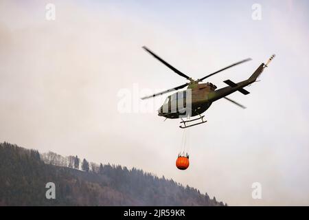 Örtlich begrenztes Wildfeuer, bei dem der Hubschrauber Wasser abtropft, indem er einen Wassereimer verwendet, der an einer langen Linie unter dem Hubschrauber befestigt ist Stockfoto