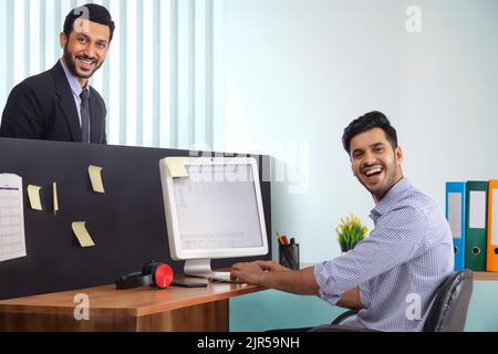 Die Mitarbeiter des Unternehmens arbeiten zusammen am Schreibtisch, wobei einer am Computer arbeitet und der andere steht. Stockfoto