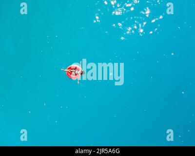 Blick von oben auf eine Frau, die auf einem aufblasbaren Ring im blauen Meerwasser schwimmt Stockfoto